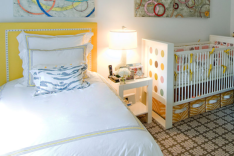 Baby room with crib next to a twin bed with upholstered yellow headboard and graphic print rug