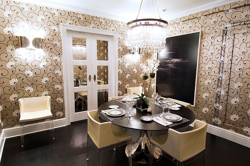 Dining room with white and tan floral wallpaper, crystal chandelier, and a tulip style table with a metal and lucite base and upholstered Philippe Starck Madeline chairs
