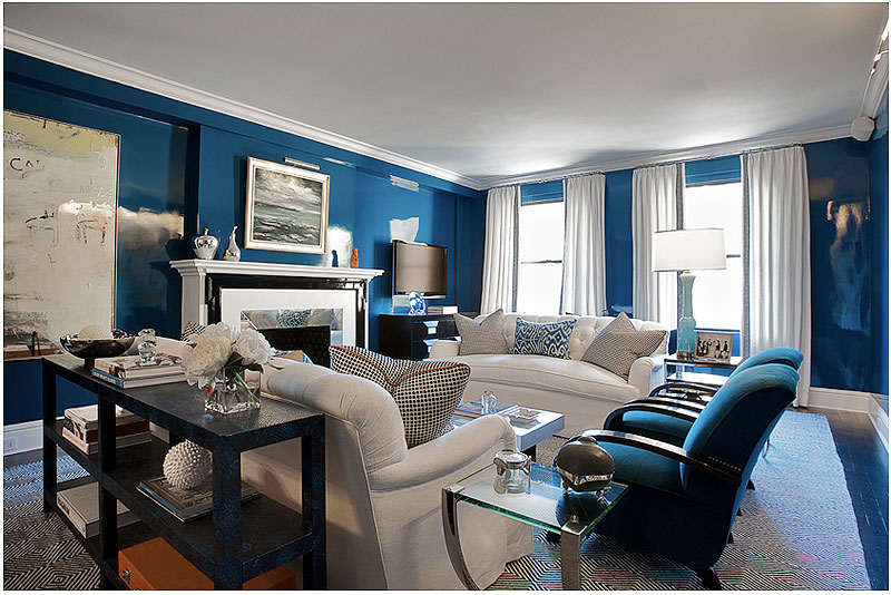 Blue living room with Madeline Weinrib ikat pillows, a tight back tufted white sofas, and a mirrored fireplace surround