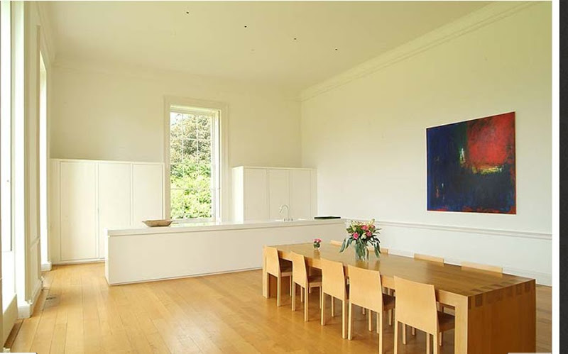 Kitchen in Wardour Castle with high ceiling wood floor, white cabinets and a long wood table