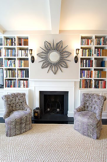 Living room with herringbone printed armchairs, a fireplace, graphic print area rug and built in bookshelves