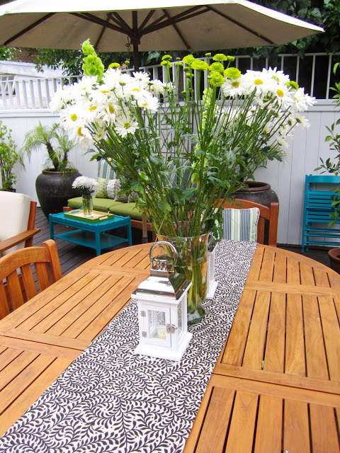 Tall  floral arrangement with white daises and pom poms on a teak patio table