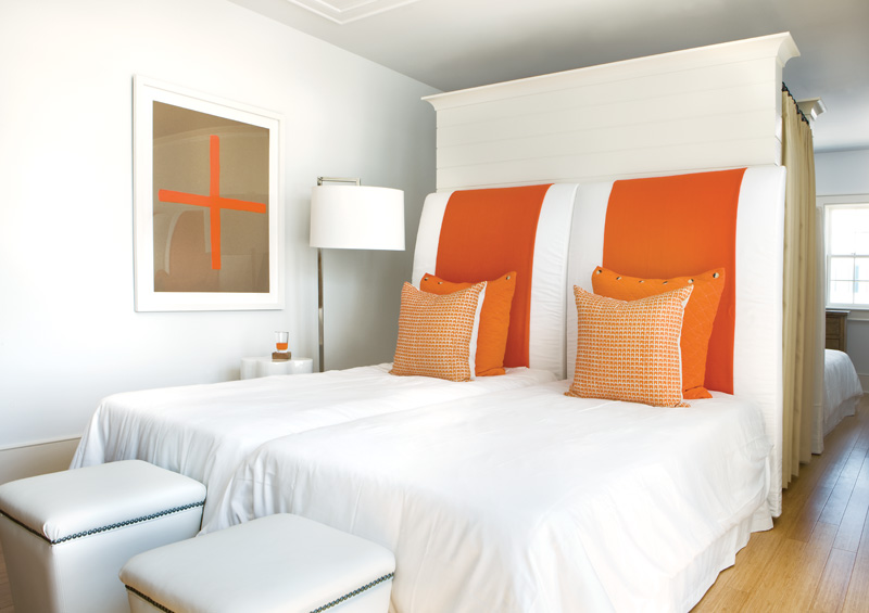 White guest bedroom in a Florida beach house with a large orange stripe on the headboard and orange accent pillows