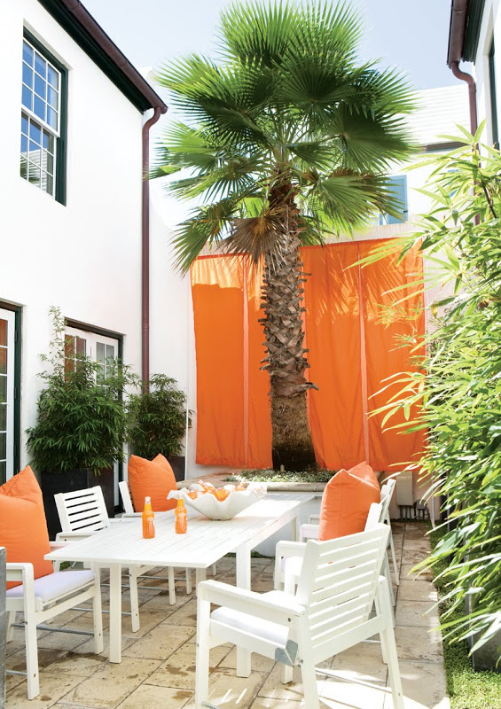Orange parachute-like drapes hang behind a grand palm tree in the outdoor dining area of a Florida beach house