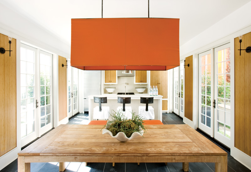 Kitchen in a Florida beach home with a large orange pendant light, orange stools, zebra wood cabinets, french doors and dark slate floor