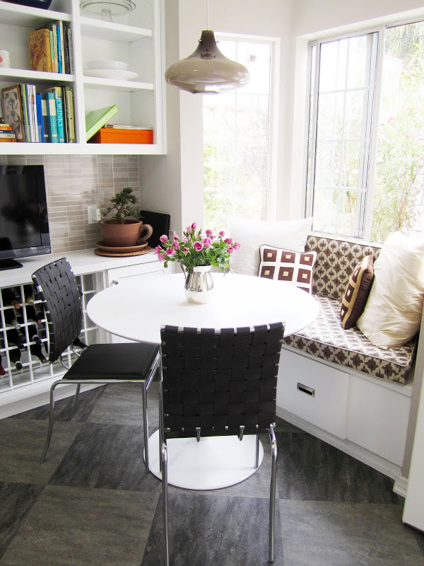 Breakfast nook with banquette seating, a pendant light and two black chairs with woven seats and backs 