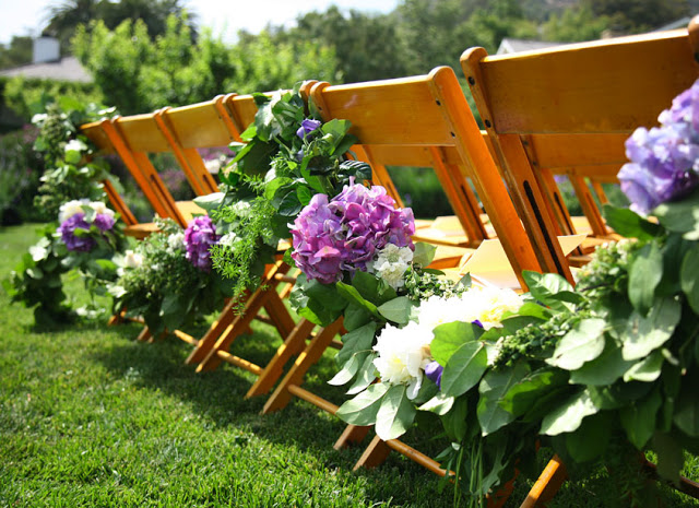  garland with purple hydrangea is draped on the backs of the chairs at a beautiful outdoor wedding