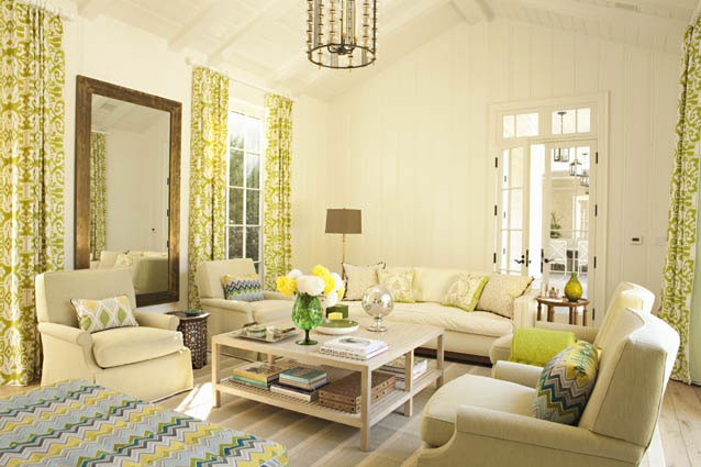 Pool house with high ceilings, exposed beams, green graphic print curtains, a large bronze mirror and cream sofas and armchairs