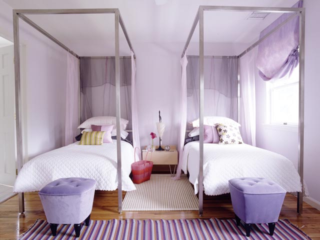 Girls bedroom with two metal canopy beds, purple ottomans at the foot of the bed and a striped rug
