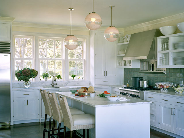 Kitchen with counter stools with a cut out on top, glass globe pendant lights hung at different heights, stainless appliances and blue tile backsplash
