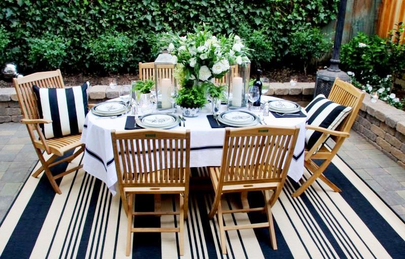 Outdoor dining party with blue and white striped rug, wood patio chairs and a blue and white table setting surrounded by a wall of ivy