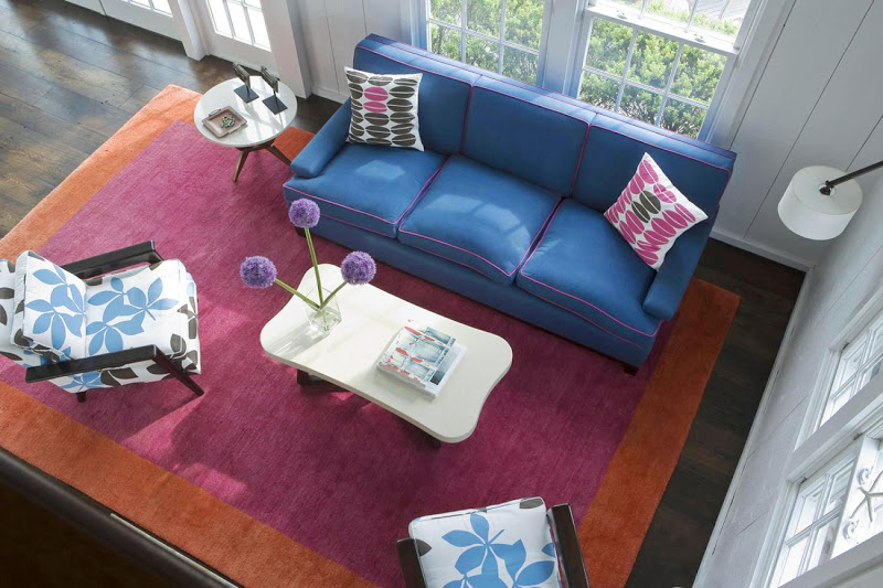 Aerial view of a living room in the Hamptons with blue sofa with pink piping, large magenta and orange area rug and two armchairs with floral cushions