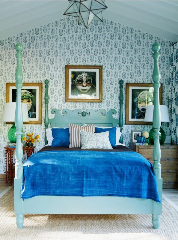 Blue bedroom by Martyn Lawrence Bullard with light blue four poster bed, blue Moroccan star lamp, blue and white wallpaper and three framed portraits
