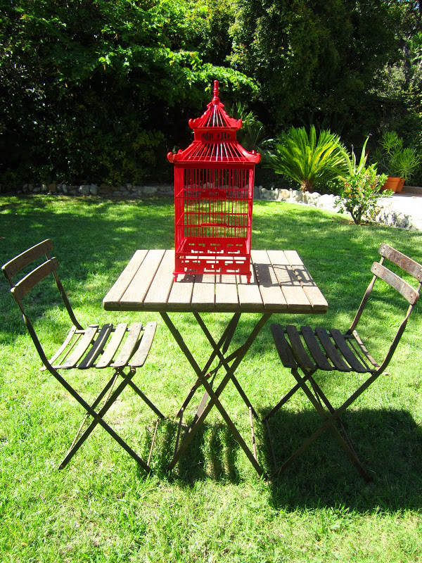 Red chinoiserie style decorative wood bird cage on an outdoor table