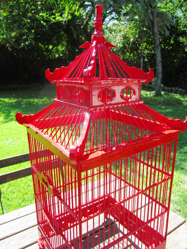 Alternative view of a red chinoiserie style decorative wood bird cage on an outdoor table