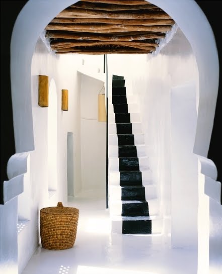 Hall with curved doorway, white stairs with black runner, log ceiling, white washed walls and a woven basket