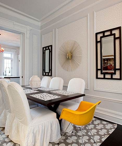 Dining room with decorative mirrors, Greek key wallpaper, slipcovered chairs and a bright yellow Eames chair