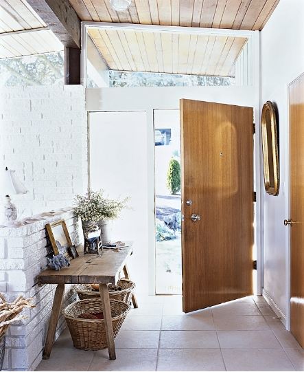 Rustic foyer with unadorned wood door and plank ceiling and white washed brick