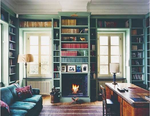 Library in an Italian villa with teal built in bookshelves, a wood floor and a blue velvet couch