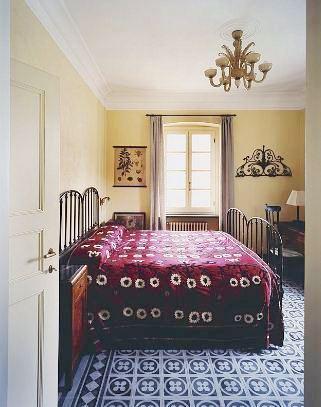 Yellow bedroom in an Italian villa with iron bed frame, chandelier and a graphic pattern rug