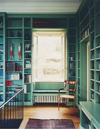 Library in an Italian villa with teal built in bookshelves and a window seat