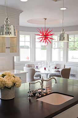 Eat in kitchen with dark countertop and two pendant lights, the breakfast nook has a tulip table and upholstered chairs under a red coral chandelier