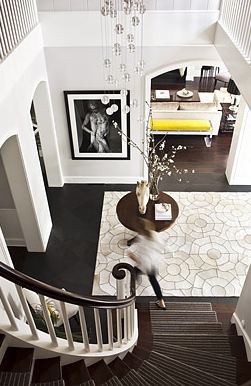 Foyer with a spiral staircase, dark wood floor, Kyle Bunting hide rug and a round table with a flower arrangement and horse head