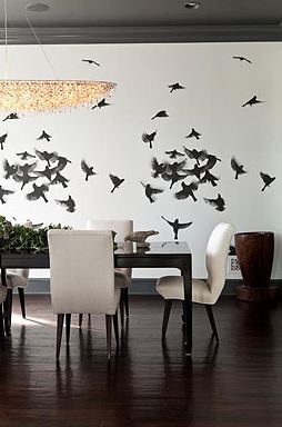 Dining room in a Pacific Palisades home with a mural of a flock of birds, dark wood floor, black table surrounded by white upholstered chairs with wood legs and a chandelier