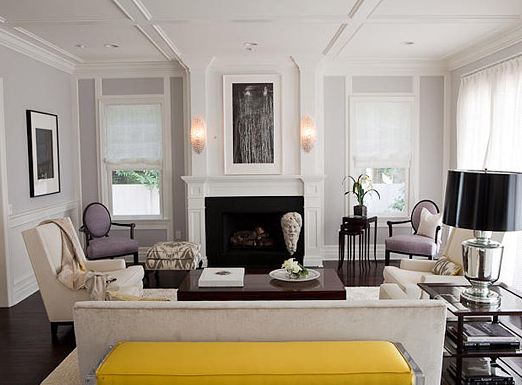 Living room in the Pacific Palisades with coffered ceiling, light grey walls, a white fireplace, dueling armchairs, a long grey sofa, dark wood floor and a bright yellow bench