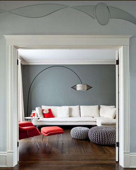 Grey living room with wood floor, grey knit poufs, white sectional sofa, red Womb Chair with matching ottoman and black arched lamp