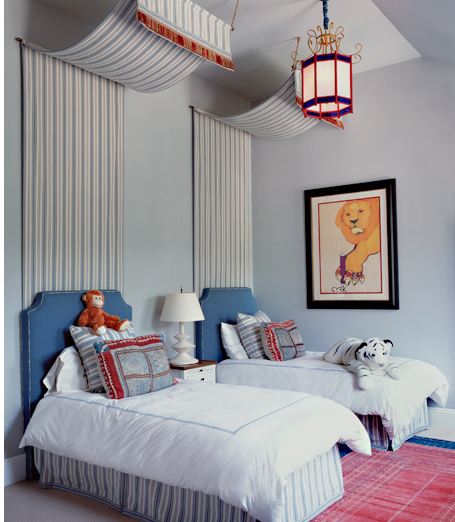 Bedroom with two twin beds with striped canopies and blue upholstered headboards, a red rug and a colorful lantern