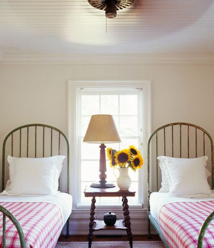 Bedroom with two twin wrought iron beds with arched headboards, red gingham bedding, beadboard ceiling and a wood nightstand between the beds