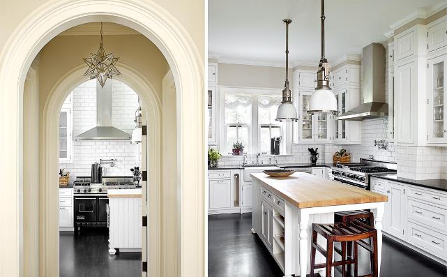 On the left is an arched entry way to a kitchen, on the right is the kitchen with subway tile from counter to ceiling, dark wood floor, white and silver pendant lights, white cabinets and drawers, black counter tops, and a white island with wood counter top