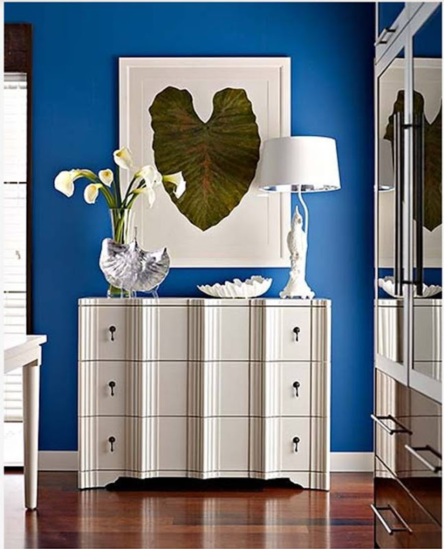 white chest of drawers leaning against a royal blue wall with a painting of a lilly pad in a white frame on the wall