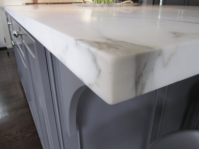Corner of a large grey island topped with Calacatta gold marble in a kitchen