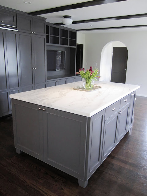 Kitchen with a large grey island topped with Calacatta gold marble, dark wood floor and grey cabinets and drawers