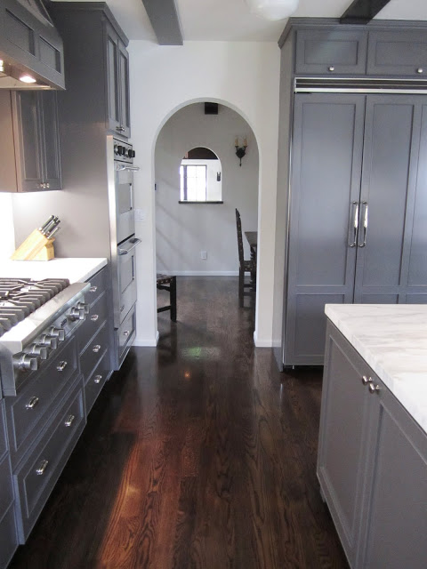 Arched entry way out of a kitchen with dark grey cabinets and drawers, marble counter tops, wood floor, and a large island with a marble top