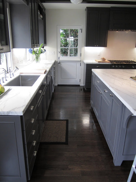 Kitchen with Dutch side door with paned window, grey cabinets and drawers, stained wood floor and marble counter tops