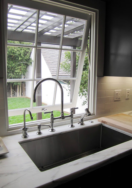 Kitchen with casement picture window, arched Kohler metal faucet and fittings, and marble counter top