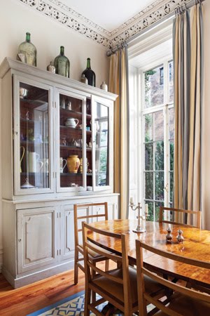 Grey dining room with high ceilings, carved moldings, a grey china cabinet, large windows and a wood table surrounded by matching chairs