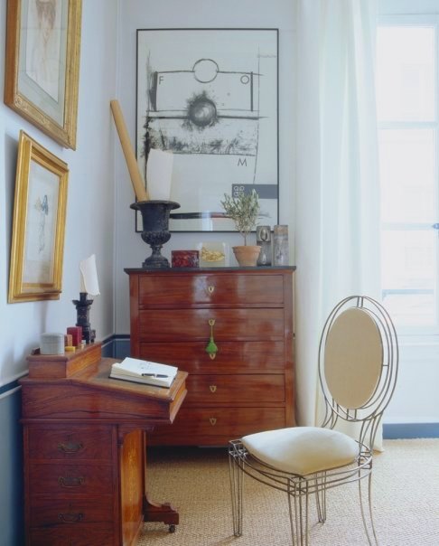 Room in a Paris apartment with a wood writing desk with a wire chair and white cushions and chest of drawers, a sisal rug and large french doors