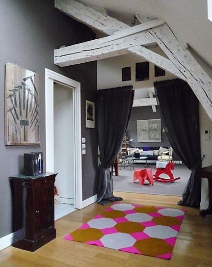 Foyer in a Paris apartment with painted white natural wood beams, grey wall, wood floor and a pink, brown and grey hexagon rug. Instead of a door to the living room, they have curtains
