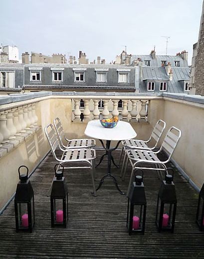 Roof top patio in Paris with metal seats, a white oval table with black metal legs and black lanterns with pink candles