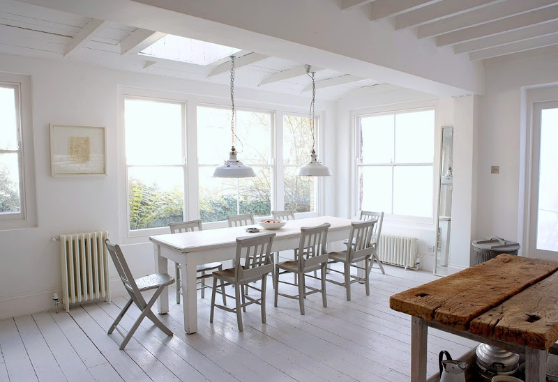 White rustic eat in kitchen with white washed floors, tables and chairs, exposed bulb lighting, and reclaimed butcher block island. 