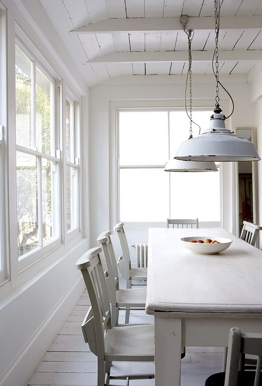 White rustic dining room with white washed floors, tables and chairs, exposed beams and white dome style pendant lights