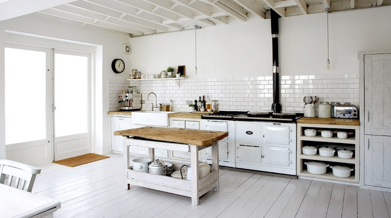 White rustic eat in kitchen with white washed floors and cabinetry, exposed bulb lighting, white subway tile backsplash with dark grout lines, and reclaimed butcher block counter tops. 