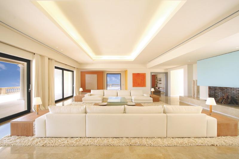 Living room in a mansion in Mallorca with large picture windows, wood floor, white dueling sofas, a shade rug and wood side tables