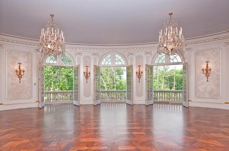 Living room with two crystal chandeliers, wood floor, french doors opening to a balcony, paneled walls, wall mounted candle holders and moulded ceiling