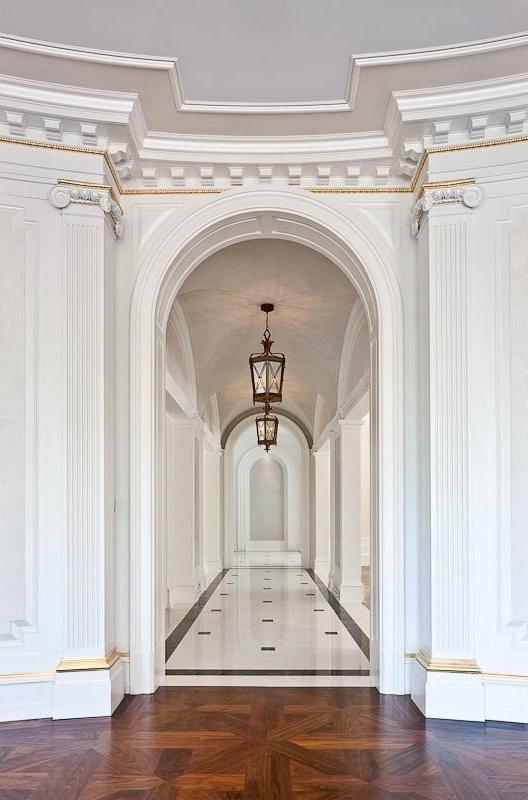 Hallway with wood floor, Greek columns, arched entryway, black and white tile floor, moulded detailing and a coffered ceiling