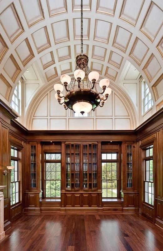 Library with arched, coffered ceiling, chandelier, wood floor and wood paneled walls and cabinets with glass doors